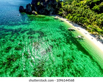 Top view of a tropical island with palm trees and blue clear water. Aerial view of a white sand beach and boats over a coral reef. The island of Palawan, Philippines.