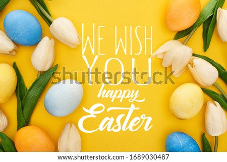 top view of tulips and painted Easter eggs on colorful yellow background with we wish you a happy Easter illustration