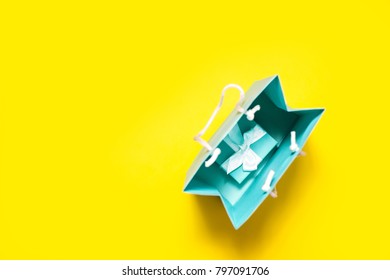 Top View Of Turquoise Gift Box With White Ribbon And Shopping Bag On Bright Yellow Background 