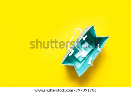 Top view of turquoise gift box with white ribbon and shopping bag on bright yellow background 