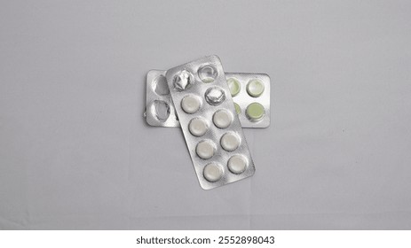 A top view of two blister packs of pills, one with white pills and the other with green pills, on a textured white surface. The packs are partially empty. Perfect for medical or pharmaceutical concept