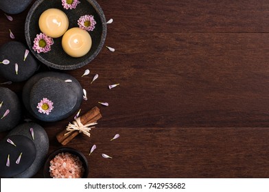 Top view of two burning candles with pink flower petals and salt on wooden background. Lastone therapy and floating candles with daisies on wooden table. High angle view of spa set with copy space.