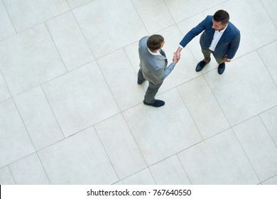 Top View Of Two Business People Shaking Hands Standing On Tiled Floor In Hall Of Modern Office Building, Copy Space