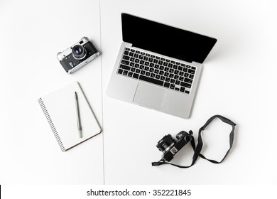Top view of two cameras, notepad with pen and blank screen laptop isolated over white background