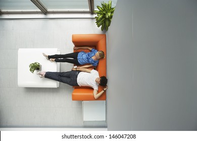 Top View Of Two Casual People Reclining On Couch In Reception Room At Office