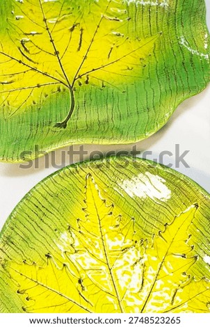 Top view of two ceramic plates with leaf imprint veins glossy yellow and green glaze on neutral surface