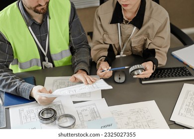 Top view at two engineers designing blueprints at workplace in office and holding machine part, copy space
