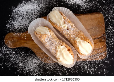 Top view of two fresh cannoli in paper on a cupboard on a black background powdered with sugar