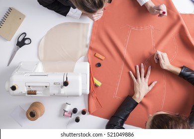 Top view of two girls making a pattern on a red piece of material. Sewing machine is standing on the table beside them. - Shutterstock ID 521049886