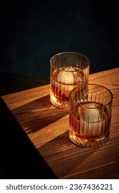 Top view of two glasses of whiskey, rum, brandy or bourbon with ice cube standing on wooden table over dark background. Concept of alcohol, strong spirits, drinks, liquid, restaurant, club, pub. Ad