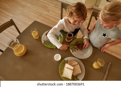 Top view of two little kids preparing breakfast for themselves in the kitchen. Cute brother spreading chocolate butter on toasted bread. Children spending time alone. Horizontal shot - Powered by Shutterstock