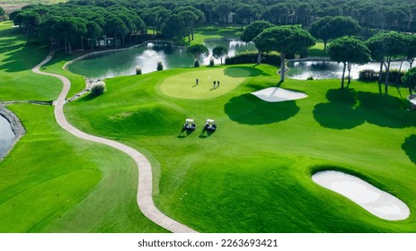 Top view of two men playing golf on a sunny summer day. Aerial view of the green golf course. Hitting the ball with a golf stick. An active type of recreation. Golf car - Powered by Shutterstock