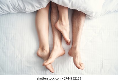 Top View Of Two Pairs Of Bare Male And Female Legs Lying Under The Blanket