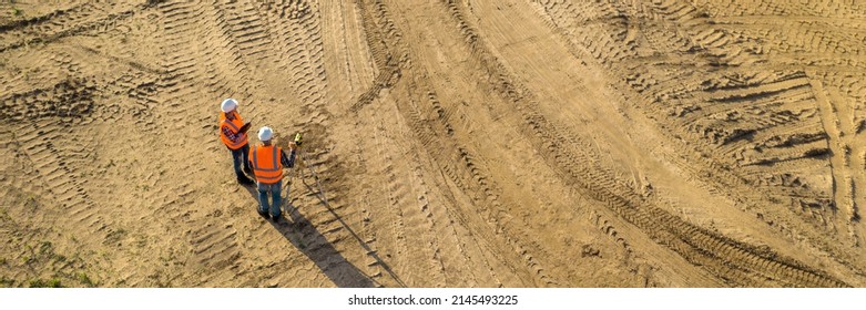 Top view of two road construction workers in orange vests and protective helmets in the middle on the field - Powered by Shutterstock