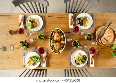 Top view of two roasted chicken in a bowl on lunch table. High angle view of dining table with salad and red wine.