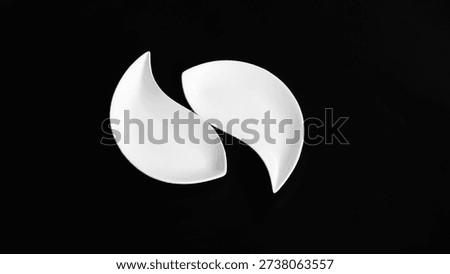 Top view of two smooth white ceramic abstract shapes arranged symmetrically on a deep black background. Minimalist composition with high contrast lighting, representing balance, harmony, modern art, and contemporary interior design aestheti