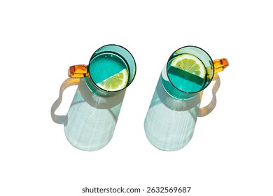 Vista superior dos vasos de color verde azulado Beber agua natural con rodajas de limón aislado sobre fondo blanco, sombra del sol y reflejo de la luz del sol, Bebida de verano en vasos de vidrio de color con asas naranjas