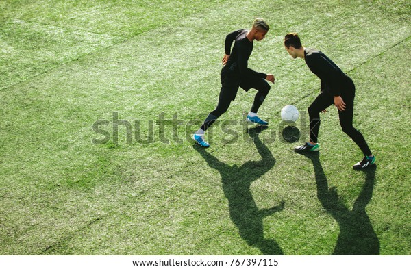 Top view of two teenagers playing football during\
team practice in field. Young soccer players playing on the sports\
grass field.