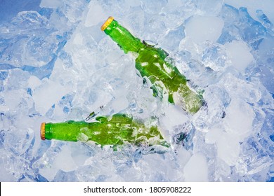 Top view of two unopened bottles of fresh beer in stack of ice cubes