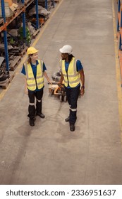 Top view of two warehouse workers pushing a pallet truck in a shipping and distribution warehouse.