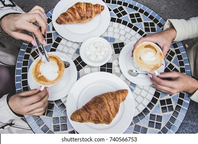 Top View Of Two Women Having Coffee Brake In French Cafe. Women Friends Drinking Coffee In French Styled Restaurant. Croissants With Coffee On Vintage Table. Girls Enjoying Coffee Outdoors.