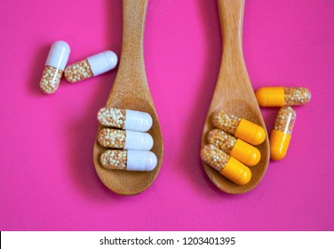 Top View Two Wooden Spoons With White And Yellow Capsules Of Vitamin C And Zinc On Pink Background. 