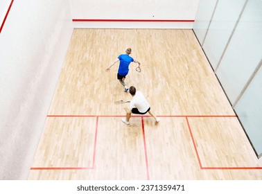 Top view of two young men, friends, sportsmen playing squash on squash court. Competition. Concept of sport, hobby, healthy and active lifestyle, game, gym, ad