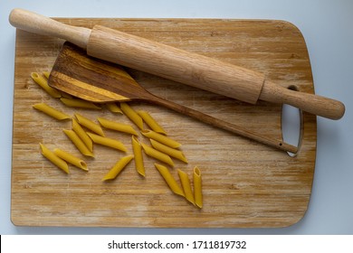 Top view of uncooked penne spaghetti with wooden rolling pin and wooden spatula on wooden cutting board - Powered by Shutterstock