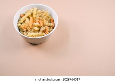 A Top View Of Uncooked Tri-color Rotini Pasta On A Bowl Isolated On Brown Background