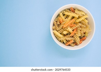 A Top View Of Uncooked Tri-color Rotini Pasta On A Bowl Isolated On Blue Background