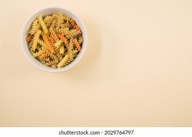 A Top View Of Uncooked Tri-color Rotini Pasta On A Bowl Isolated On Light Brown Background