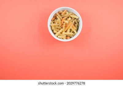 A Top View Of Uncooked Tri-color Rotini Pasta On A Bowl Isolated On Pink Background