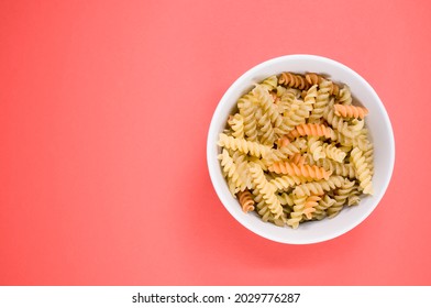 A Top View Of Uncooked Tri-color Rotini Pasta On A Bowl Isolated On Pink Background