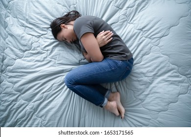 Top view of unhappy depressed young woman lying on bed suffer from abortion or miscarriage, upset female hunch crook in bedroom sleep having emotional breakdown or crisis, healthcare concept