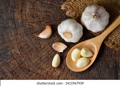 Top view of Unpeeled Garlic Cloves in wooden spoon with Bulb on old wood background. - Powered by Shutterstock