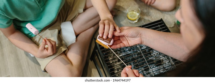 Top View Of Unrecognizable Family Making Smores With Small Barbecue At Home