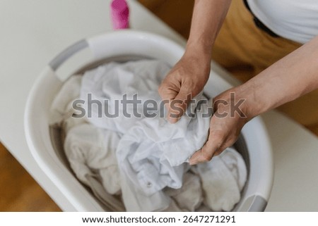 Top view of unrecognizable man preparing white clothes for washing, soaking in basin with stain remover before putting them in washing machine for perfect laundry. Concept of household cleanliness.