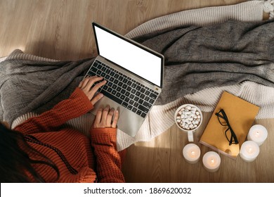 Top view of unrecognizable woman wearing a knitted sweater using laptop with copy space on the screen in home interior background. Mockup can be used to add any advertisement, texts, and graphics