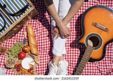 Top View Of Unrecognizable Young Woman In White Pants Outside Having Picnic, Eating And Playing Guitar. Summer Fun And Leisure