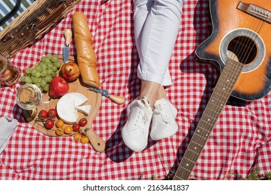 Top View Of Unrecognizable Young Woman In White Pants Outside Having Picnic, Eating And Playing Guitar. Summer Fun And Leisure