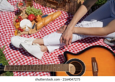 Top View Of Unrecognizable Young Woman In White Pants Outside Having Picnic, Eating And Playing Guitar. Summer Fun And Leisure