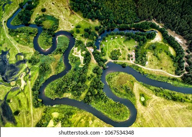 Top view of the valley of a meandering river among green fields and forests