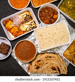 Top View Of A Variety Of Indian Takeout Food In Plastic Containers On A Fabric Background. 