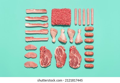 Top view with a variety of raw meat symmetrically arranged on a green-mint table. Food knolling with the ingredients for a barbecue, from sausages to the steaks.