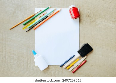 A top view of various art supplies, including colored pencils, glue, paintbrush, and a jar of paint, surrounding a blank sheet of paper. The setup is ideal for creative projects, educational activity - Powered by Shutterstock