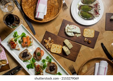 Top view of various bruschettas with different toppings, like salmon, pate and beef on white long platter. Cheese platter and baked oisters Snack finger food meal for wine, starter.
