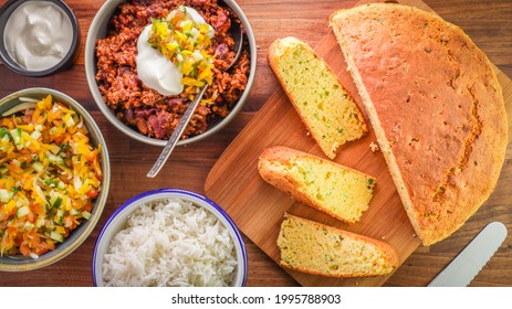 A Top View Of Various Delicious Meals On A Wooden Table Including Corn, Bread And Chili