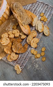 Top View Of Various Fresh Bakery Goods On Rattan Mat On Wooden Table.