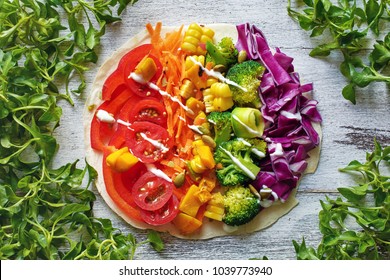 Top View Of Vegetarian Pizza With Rainbow Colored Vegetables, Seeds, Yogurt Sauce And Pitta Bread On White Table.