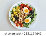 Top view of a vibrant plate of fresh Nicoise salad featuring colorful ingredients including soft-boiled eggs, tender green beans, cherry tomatoes, black olives, flaky tuna, and boiled potatoes